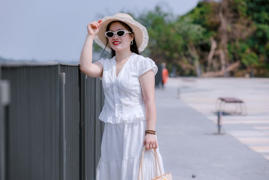 Elegant summer vacation outfit accessories on a resort balcony, featuring hat, sunglasses, and gold earrings