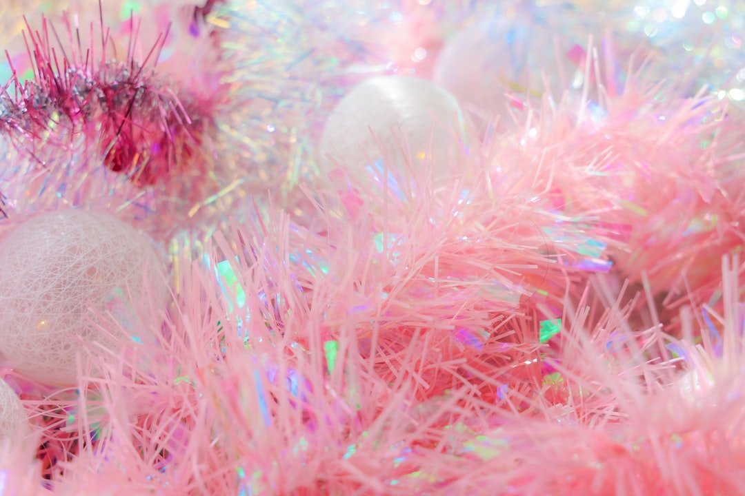Close-up of pink glitter Christmas nails with cuticle oil application, surrounded by holiday wrapping paper and ribbons