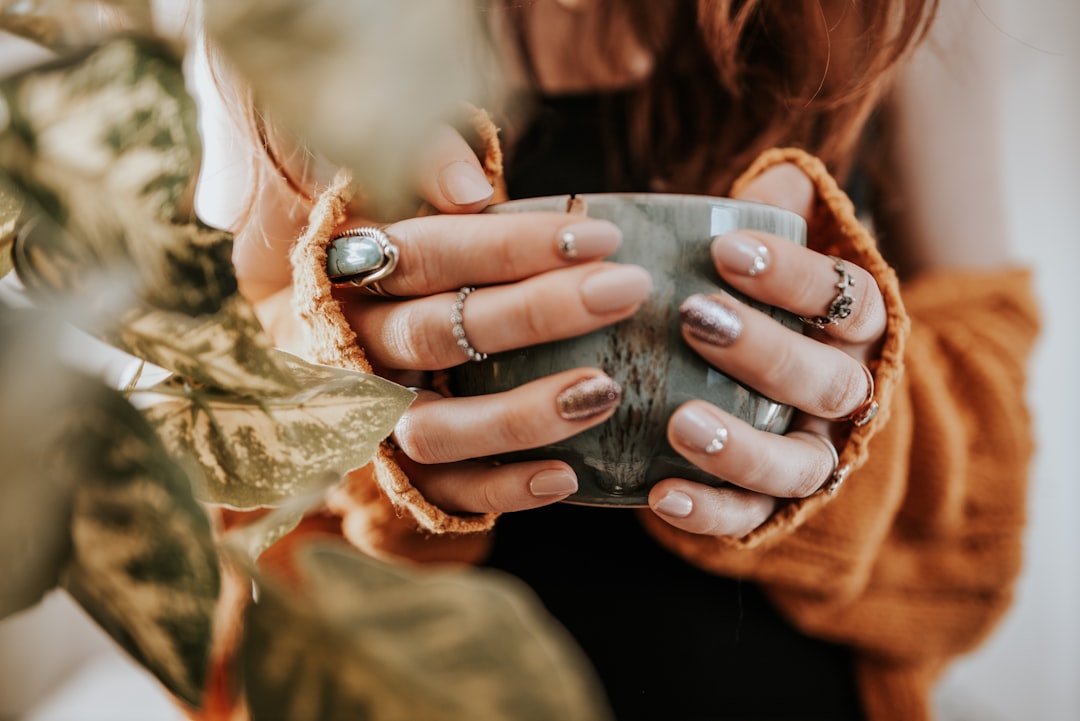 Nude minimalist fall floral nails with a small white daisy accent on the ring finger, styled with a laptop and coffee cup