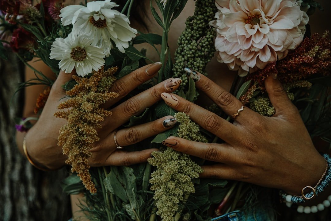 Vintage-inspired fall floral nails in earthy tones with retro floral wallpaper-style patterns, styled against a corduroy jacket