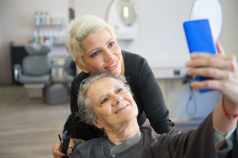 Two women, one hairstylist and one customer, taking a selfie at a beauty salon.